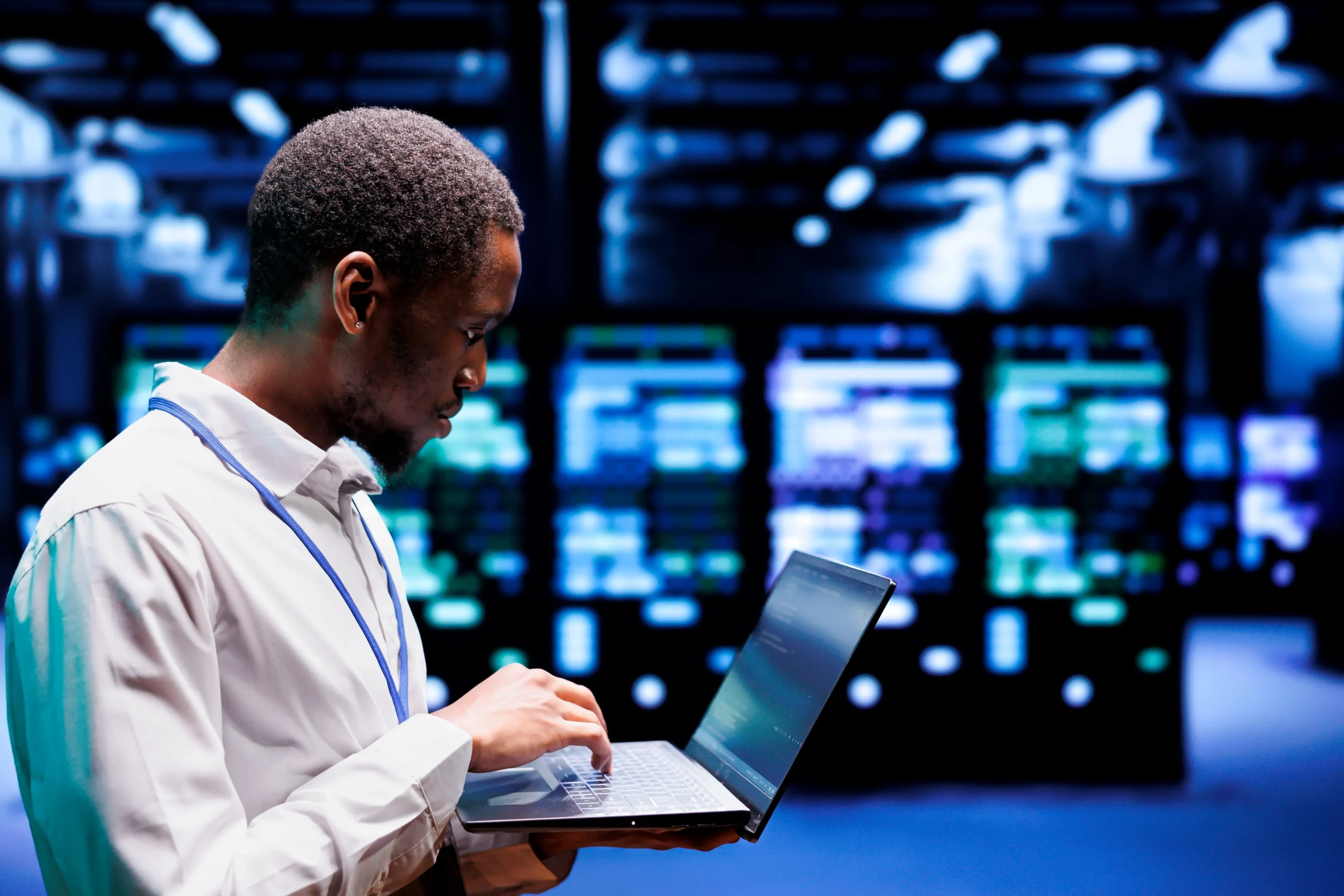 A person in a white shirt using a laptop stands in front of illuminated computer servers in a data center.
